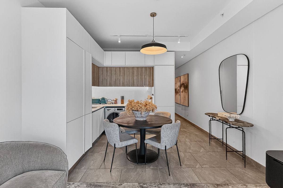 Modern open-plan kitchen and dining area featuring sleek white cabinetry, wood-tone accents, integrated appliances, and large format floor tiles.