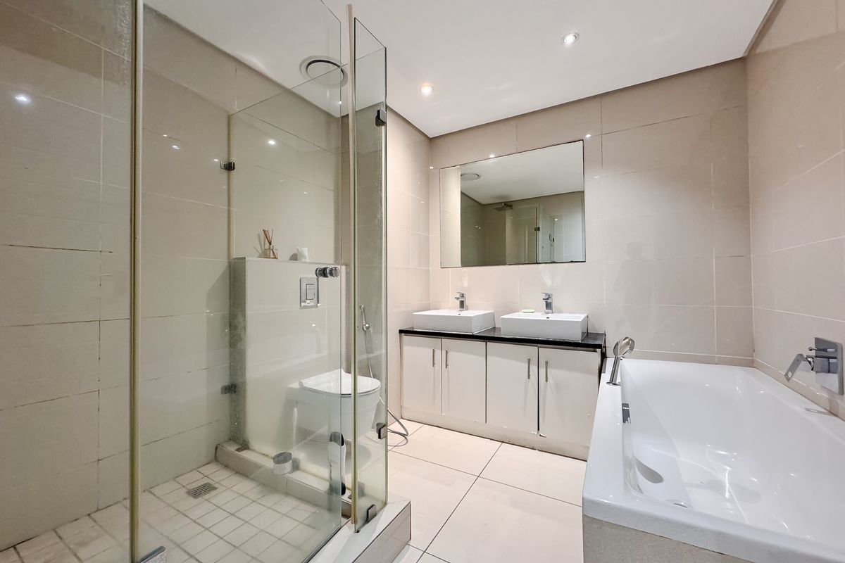 Modern bathroom featuring a glass-enclosed shower, a deep soaking bathtub, and a double vanity with integrated sinks and storage cabinetry.