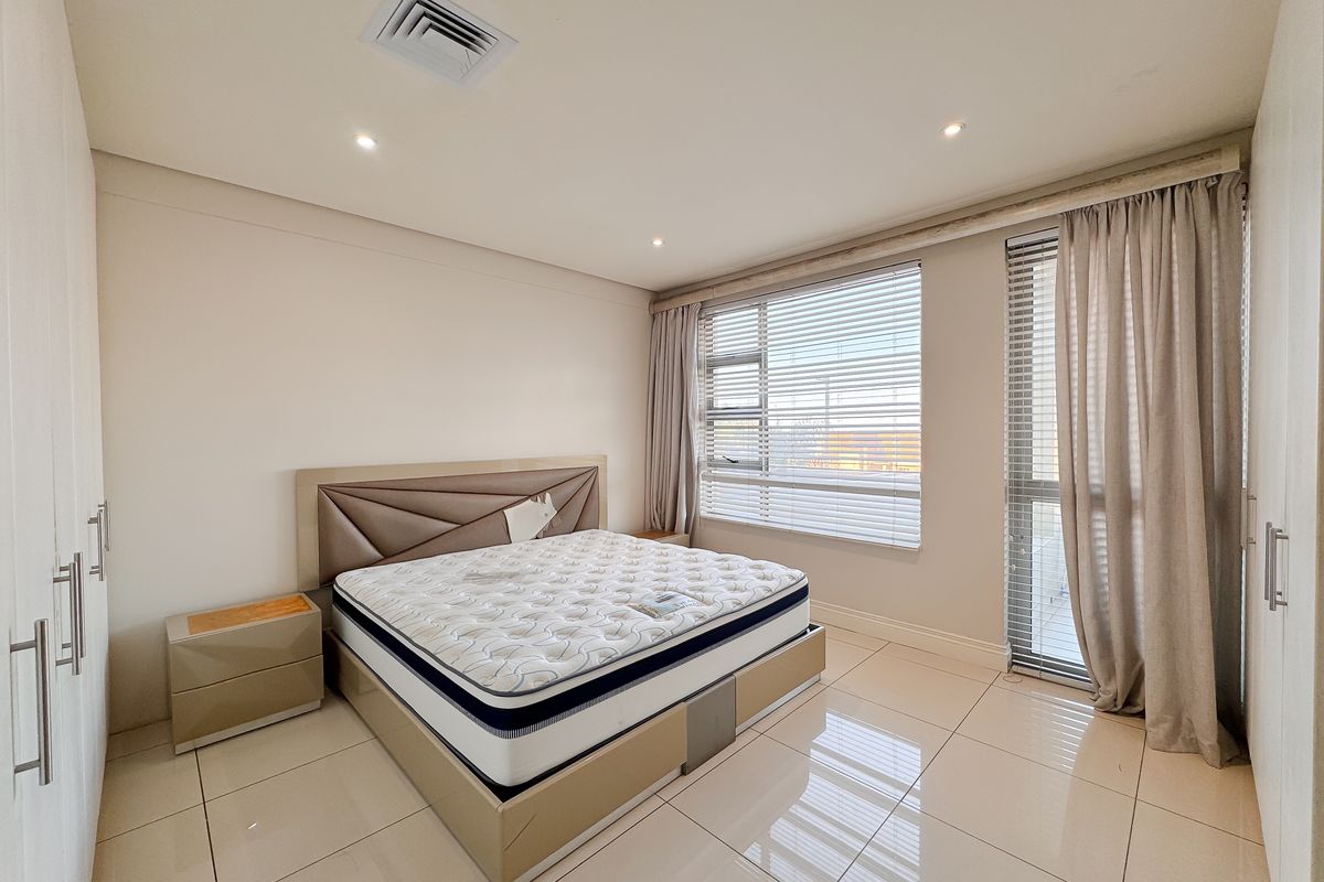 Spacious bedroom featuring large format floor tiles, built-in cupboards, recessed ceiling lighting, and ducted air conditioning with access to a private balcony.