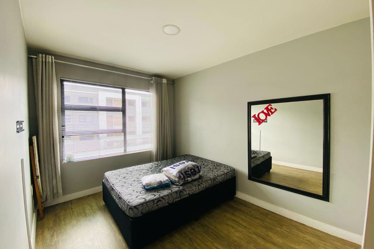 A well-maintained bedroom featuring wood-look flooring, neutral walls, and a large window with fitted blinds, providing a bright and functional living space.