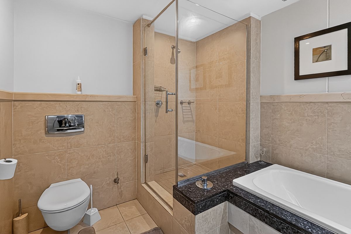 Modern bathroom featuring a glass-enclosed shower, a separate bathtub with a dark stone surround, and a wall-mounted toilet.