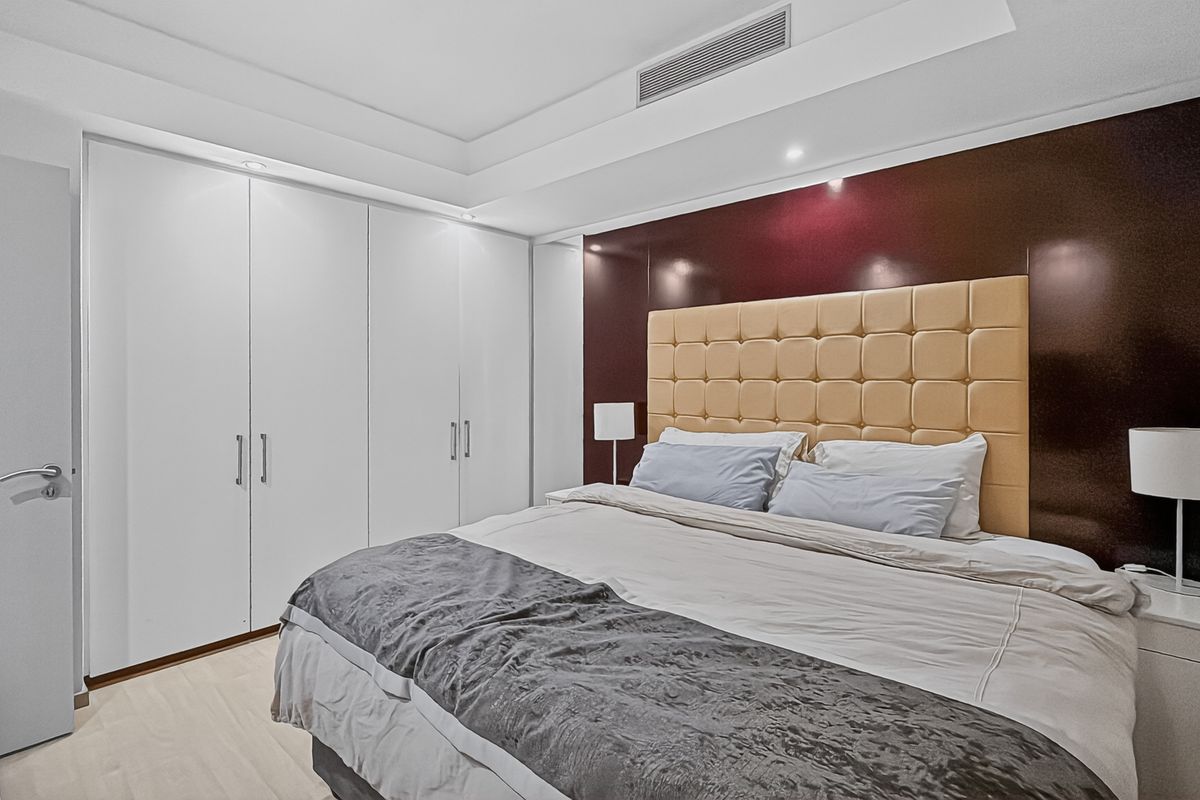 A modern bedroom featuring built-in floor-to-ceiling wardrobes, recessed ceiling lighting, and a dark feature wall panel.