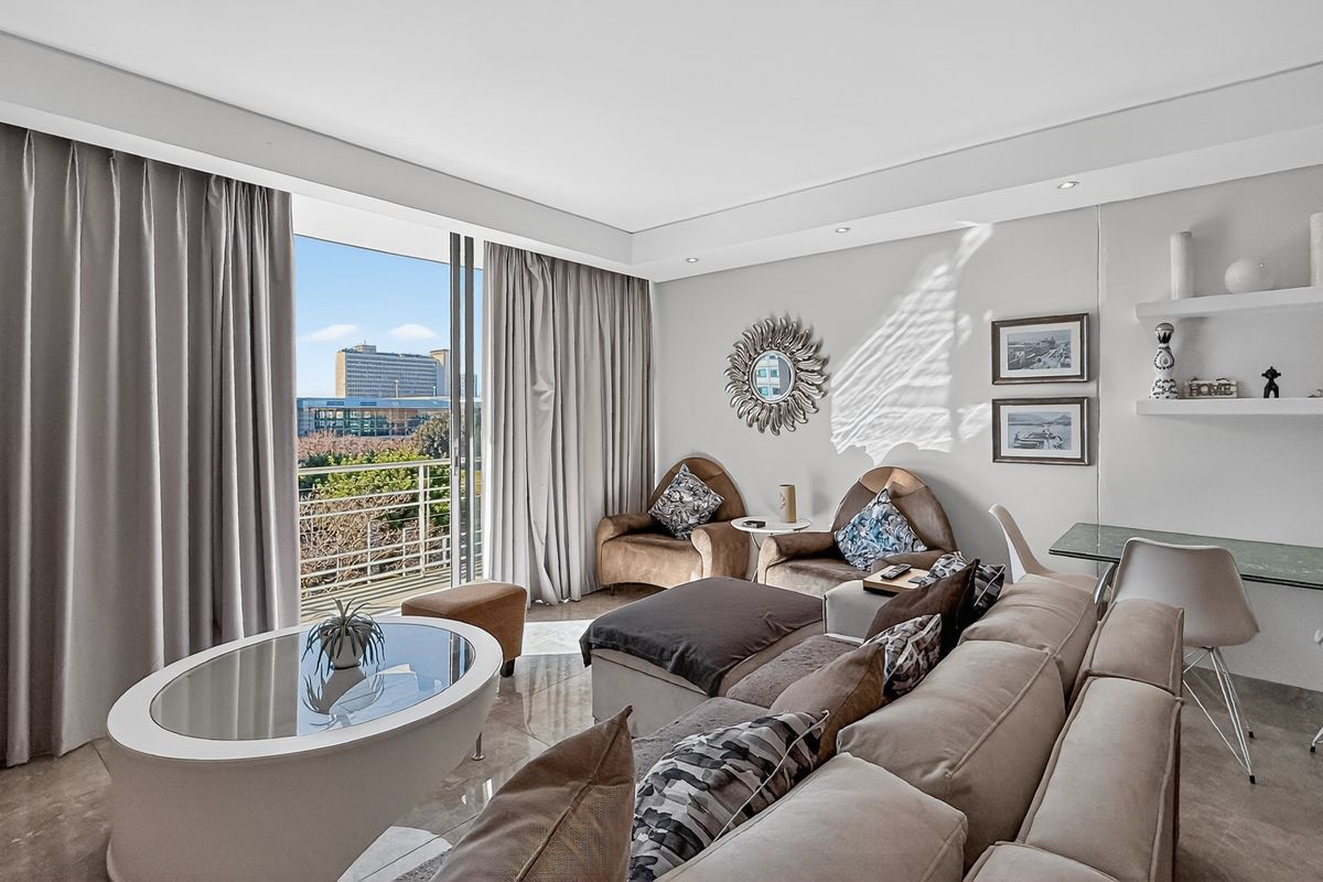 A bright and modern living room featuring large sliding glass doors that open to a balcony with city views and recessed ceiling lighting.