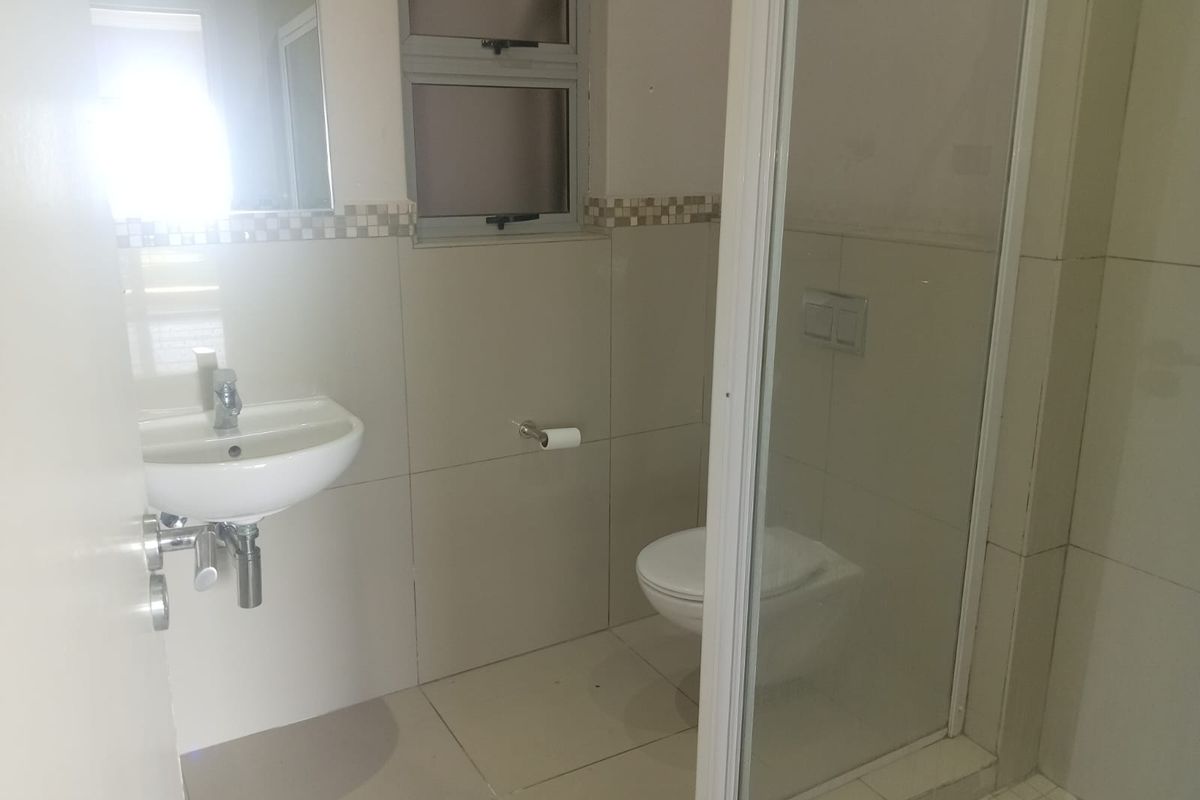 A functional bathroom featuring a wall-mounted toilet, glass shower enclosure, and a pedestal basin with neutral wall and floor tiling.