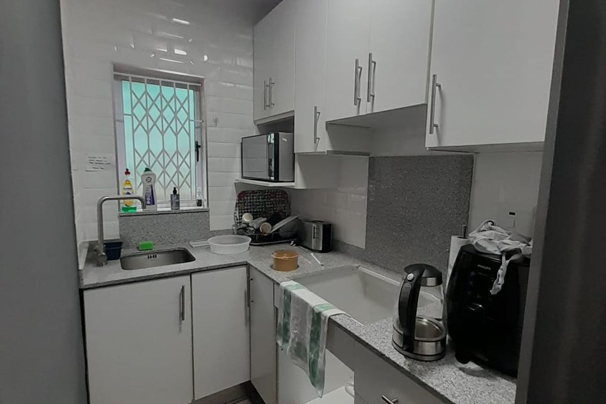 Compact kitchen featuring white cabinetry, granite-look countertops, stainless steel sink, and a security gate on the window.