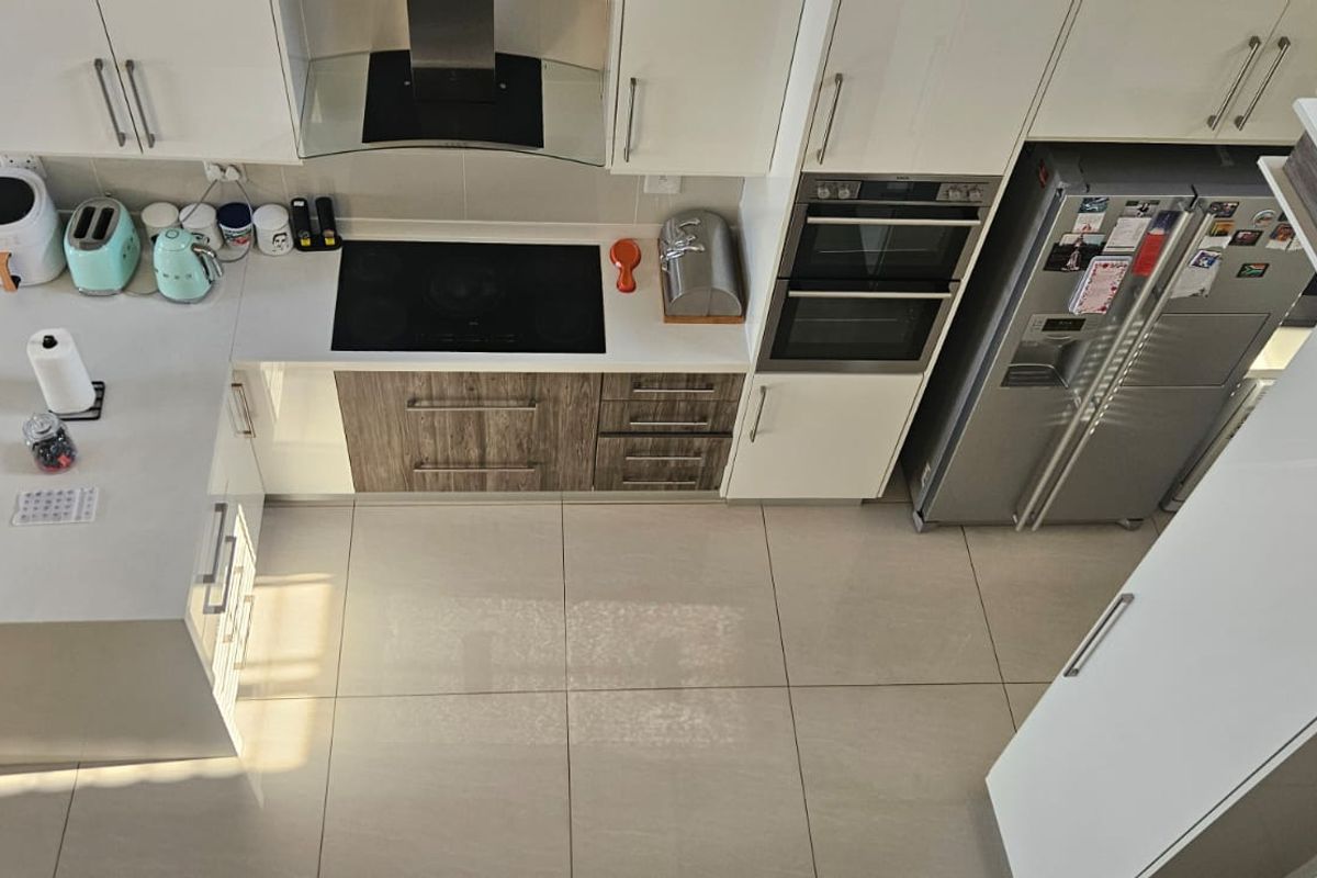 Modern kitchen featuring high-gloss cabinetry, a built-in double oven, electric hob with extractor fan, and large format floor tiles.
