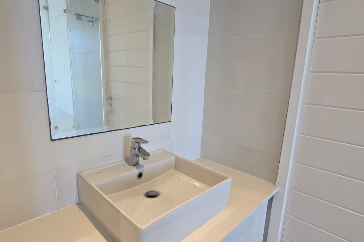 A clean, modern bathroom vanity featuring a square vessel sink, chrome faucet, and a wall-mounted mirror with neutral tiled walls.