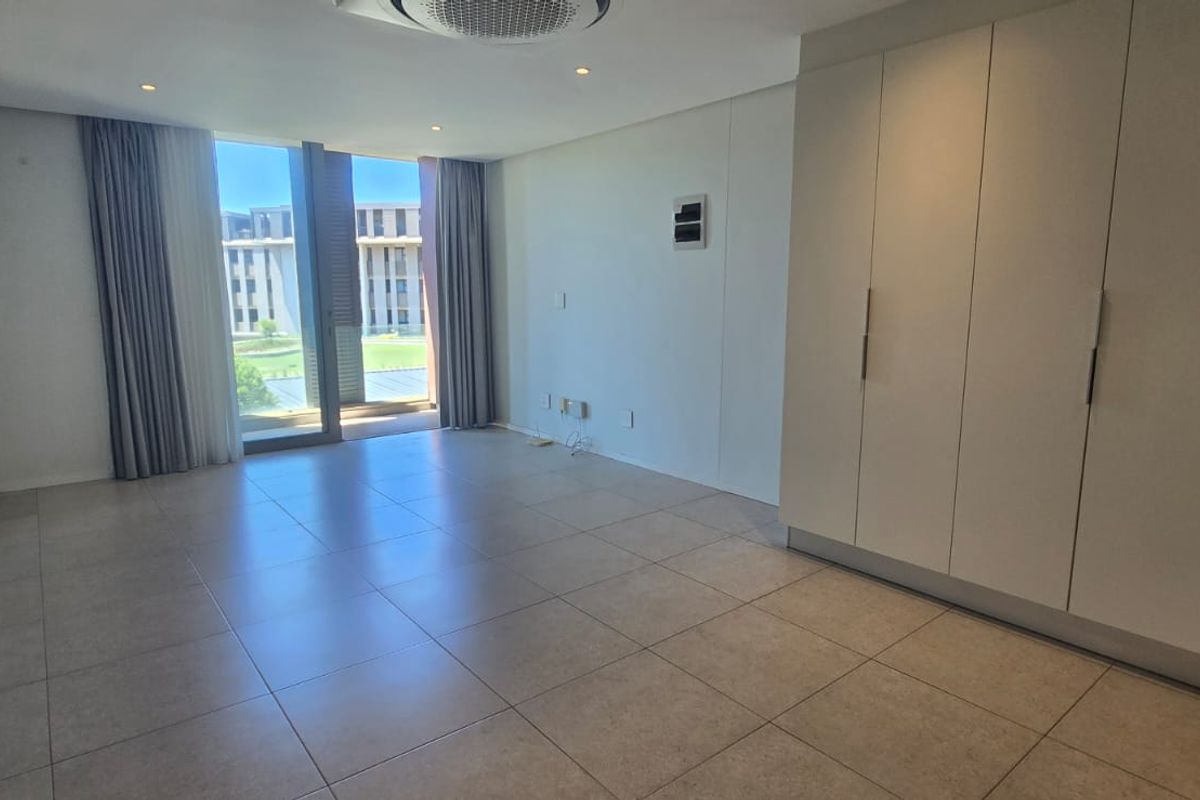 A bright and spacious bedroom featuring large format floor tiles, built-in wardrobes, and direct access to a balcony with natural light.