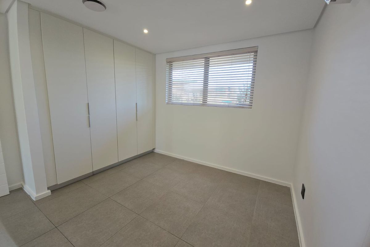 A bright, modern bedroom featuring neutral floor tiles, built-in floor-to-ceiling cabinetry, and venetian blinds.
