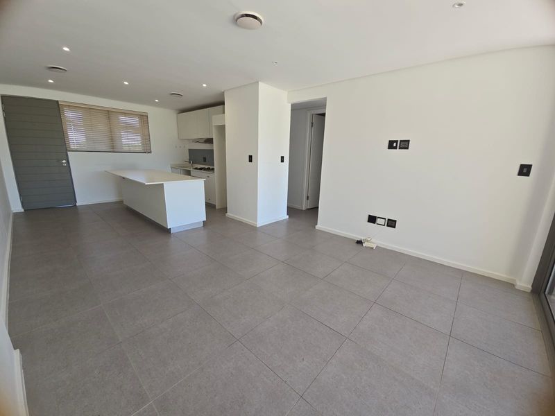 An open-plan living and kitchen area featuring modern tiled flooring, recessed downlighting, and a functional kitchen island with built-in cabinetry.