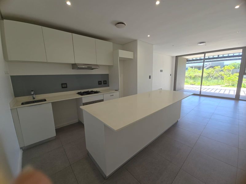 Modern open-plan kitchen featuring a central island, sleek white cabinetry, built-in gas hob, extractor fan, and tiled flooring, leading to a bright living area.
