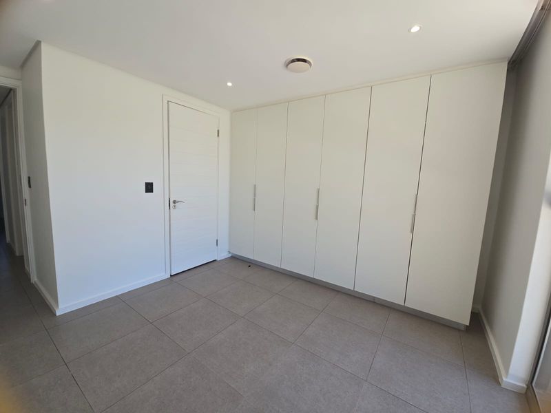 A bright, modern bedroom featuring neutral floor tiles and extensive built-in floor-to-ceiling cabinetry with a clean, minimalist aesthetic.