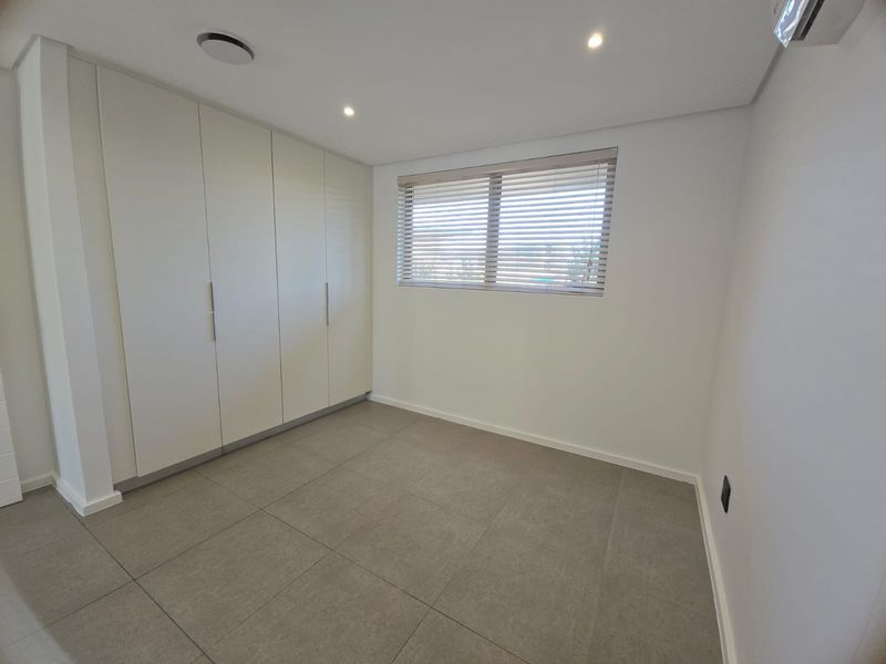 A bright, modern bedroom featuring neutral floor tiles, built-in floor-to-ceiling cabinetry, and venetian blinds.