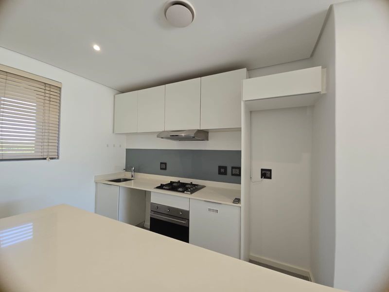 Modern kitchen featuring white cabinetry, stone countertops, a built-in gas hob, oven, extractor fan, and a dedicated space for a refrigerator.