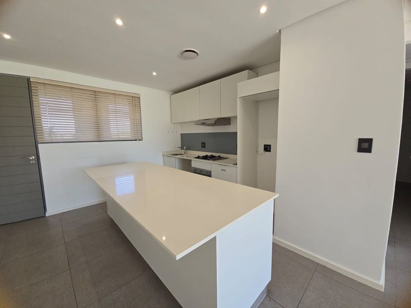Modern kitchen featuring a central island, stone countertops, built-in gas hob, extractor fan, and sleek cabinetry with tiled flooring.