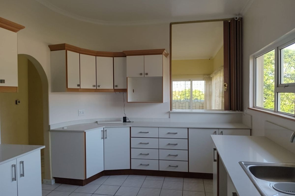 A functional kitchen featuring white cabinetry with wood trim, tiled flooring, and a large serving window connecting to the adjacent living space.