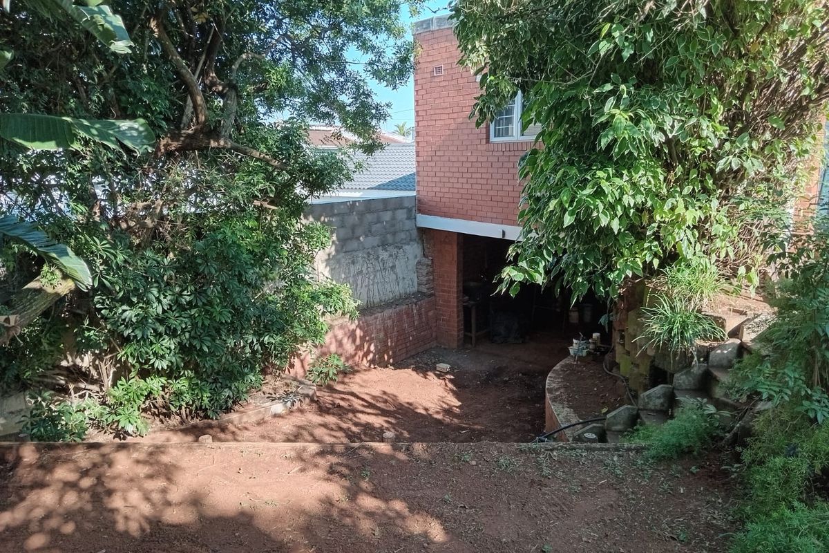 A view of the rear exterior area featuring a brick building facade, mature trees, and an unlandscaped garden space.