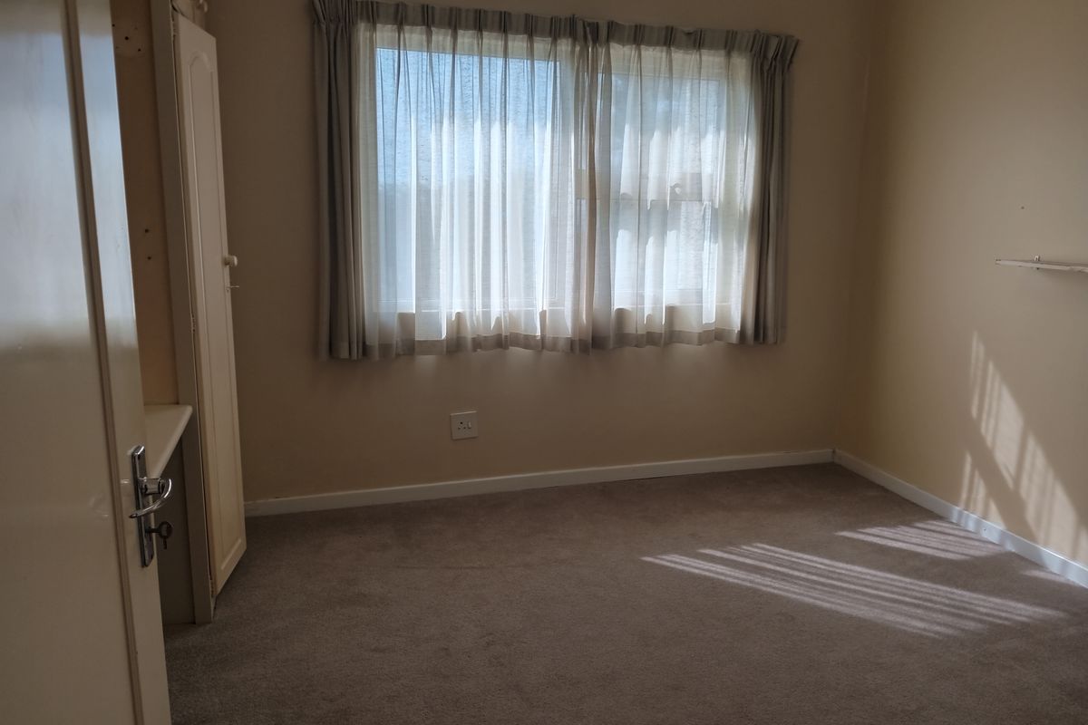 A neutral-toned bedroom featuring built-in cabinetry, carpeted flooring, and natural light through a window with curtains.