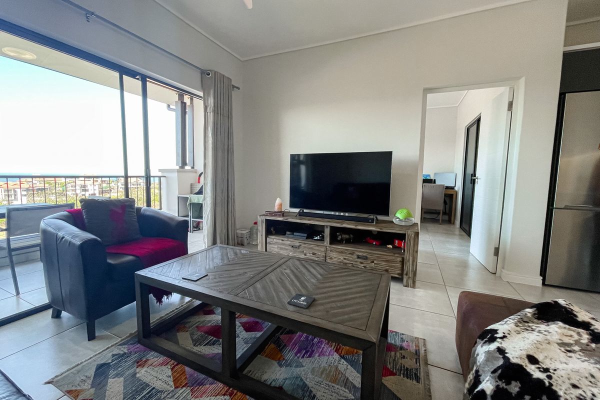 A bright living room featuring large sliding glass doors that open onto a balcony, with tiled flooring and neutral wall finishes.