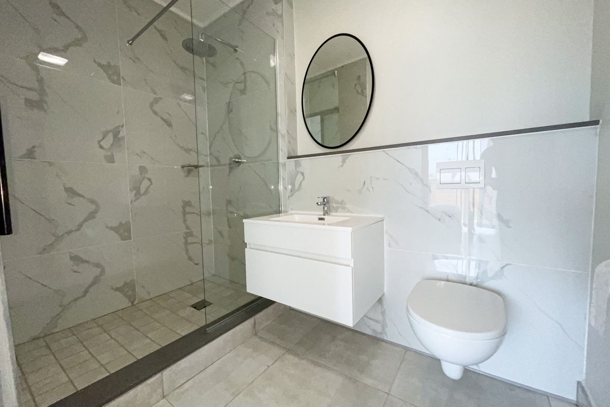 Modern bathroom featuring a walk-in glass shower, wall-mounted vanity with basin, and a wall-hung toilet, finished with elegant marble-look wall tiles.
