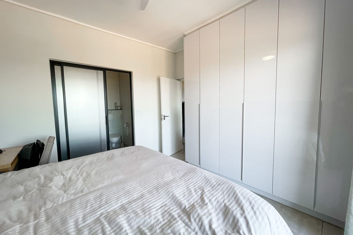 A bright bedroom featuring floor-to-ceiling built-in wardrobes and an en-suite bathroom with a sliding glass door.