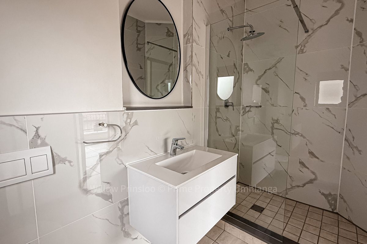 Modern bathroom featuring marble-look wall tiles, a floating vanity with integrated basin, and a glass-enclosed walk-in shower with a rainfall showerhead.