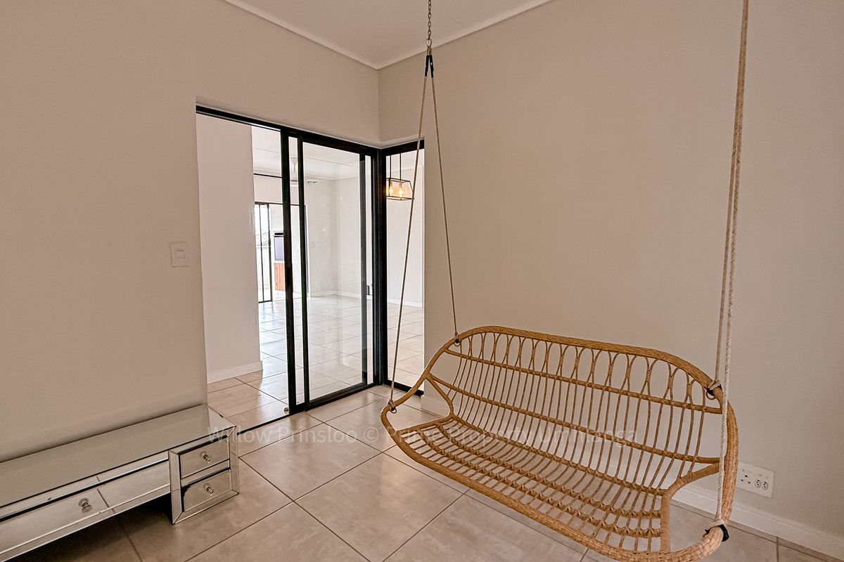 A bright living area featuring neutral tiled flooring and a modern black-framed sliding glass door leading to an adjacent room.