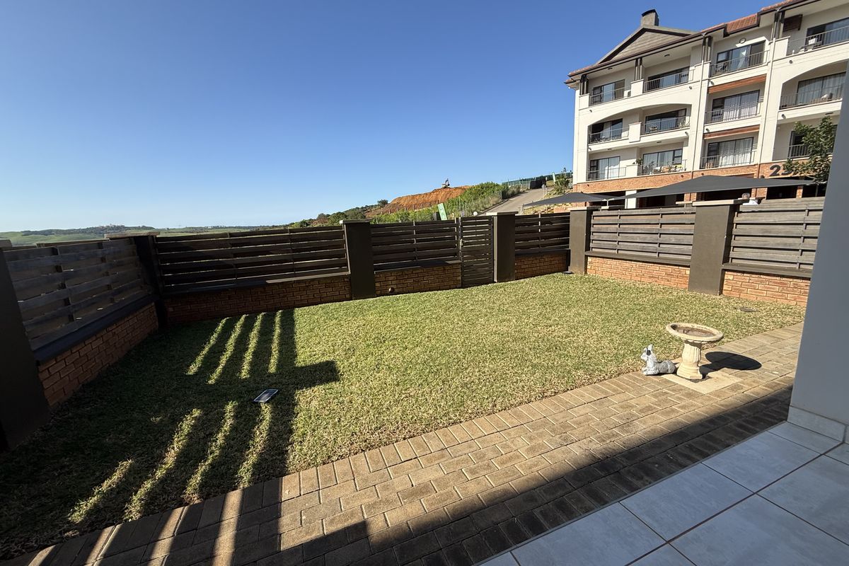 A private rear garden featuring a paved patio area, well-maintained lawn, and secure perimeter fencing with brick pillars.