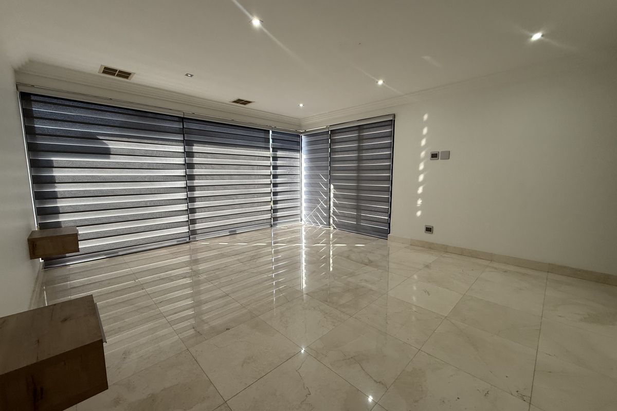A bright, spacious living room featuring polished marble flooring, recessed downlighting, and modern dual-layer roller blinds on large windows.