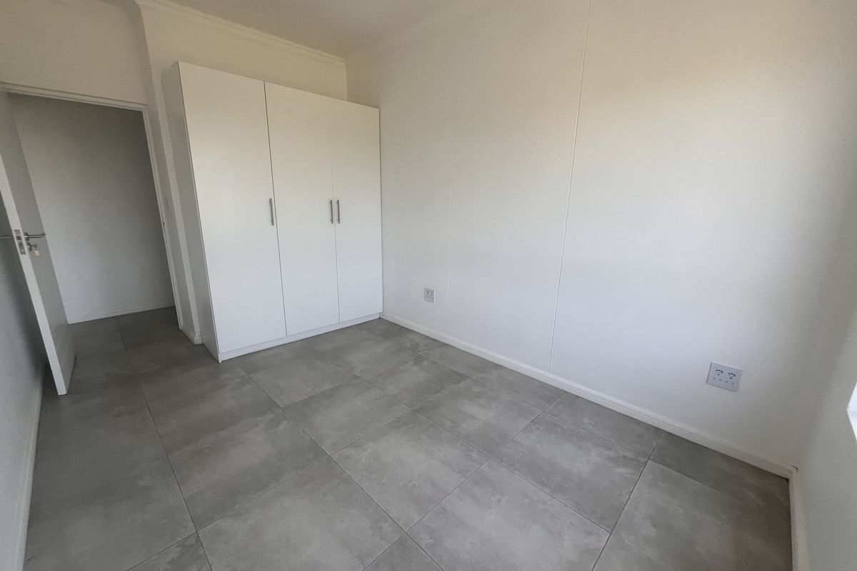 A clean, empty bedroom featuring modern grey floor tiles and a built-in white wardrobe.