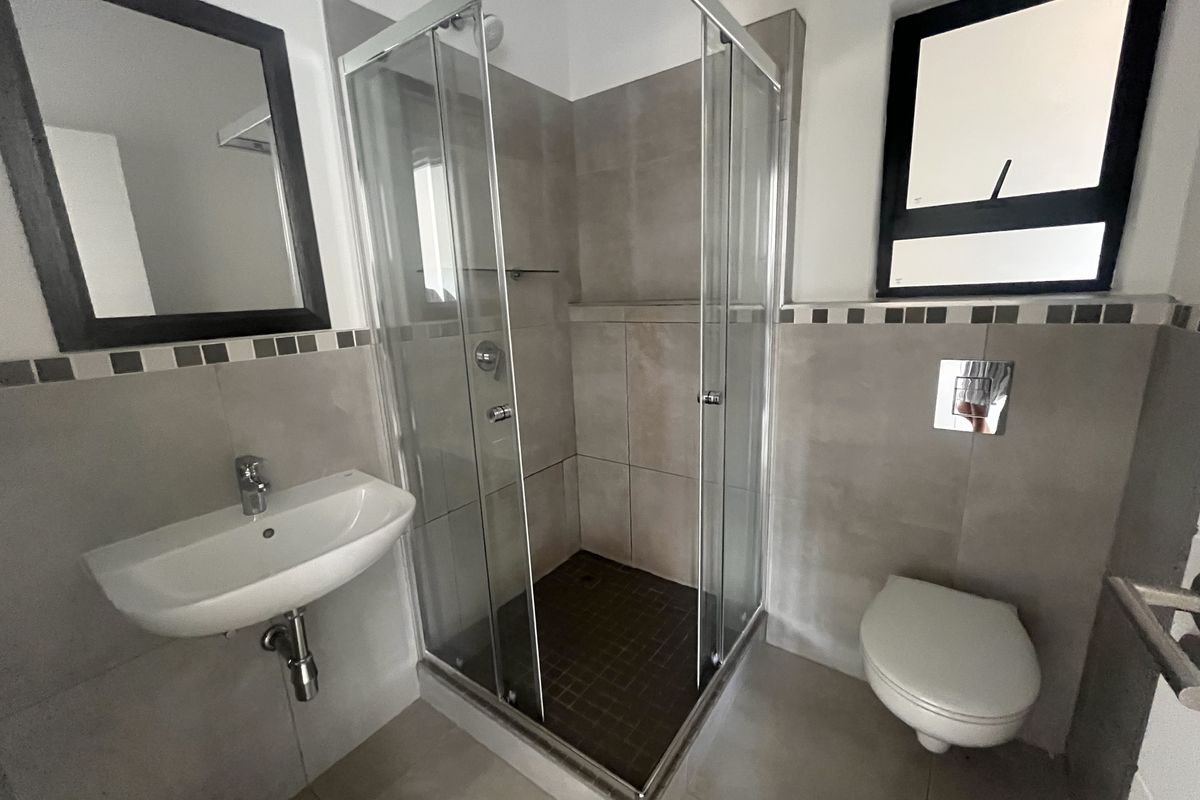 Modern bathroom featuring a glass-enclosed shower, wall-mounted basin, and a concealed cistern toilet with neutral floor-to-ceiling tiling.