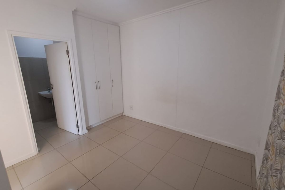A clean, empty bedroom featuring neutral floor tiles, built-in cupboards, and direct access to an en-suite bathroom.