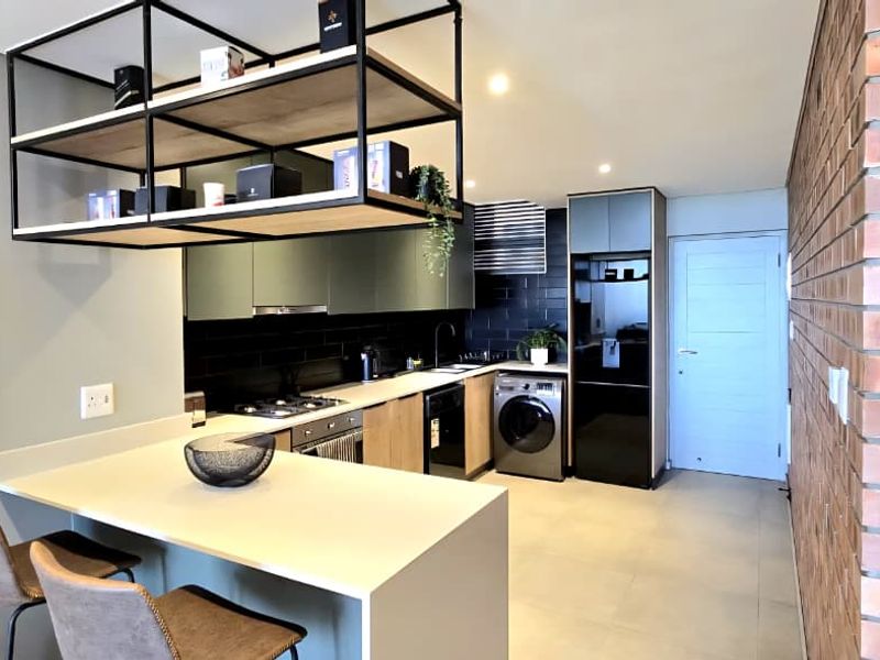 Modern kitchen featuring a breakfast bar, stone countertops, built-in oven, gas hob, and stylish exposed brick wall with integrated cabinetry and recessed lighting.
