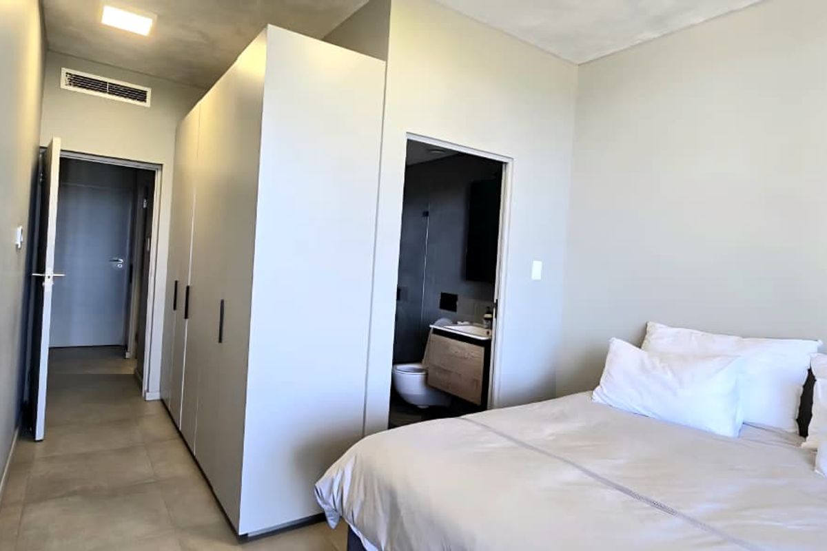A modern bedroom featuring built-in cupboards, tiled flooring, ducted air conditioning, and direct access to an en-suite bathroom.