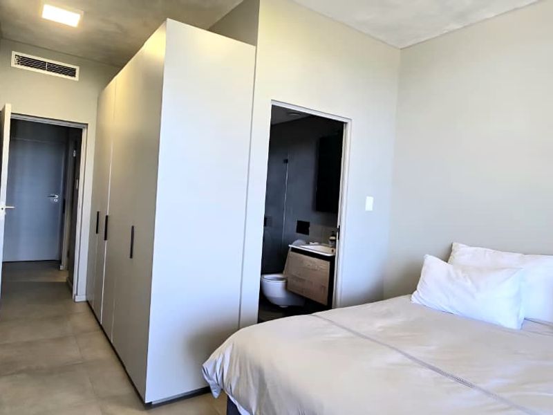 A modern bedroom featuring built-in cupboards, tiled flooring, ducted air conditioning, and direct access to an en-suite bathroom.