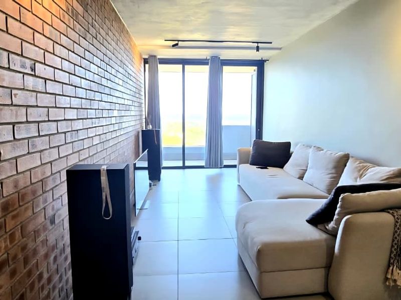 Modern living room featuring an exposed brick accent wall, large format floor tiles, and sliding glass doors leading to a balcony.