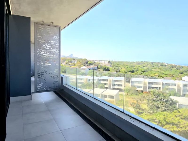 A modern, spacious balcony featuring a sleek glass balustrade, decorative privacy screen, and expansive views of the surrounding landscape and coastline.