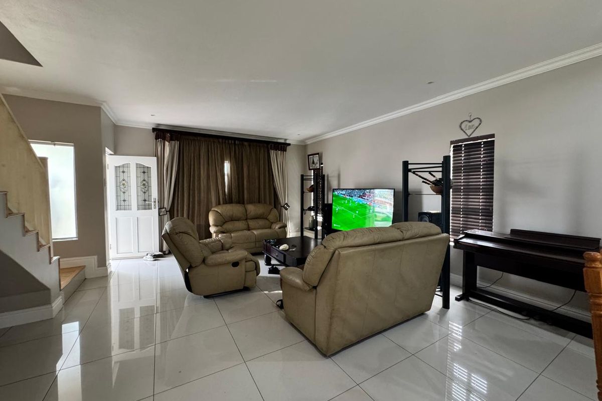 Spacious living room featuring polished porcelain floor tiles, crown molding, and a staircase with a wooden balustrade.