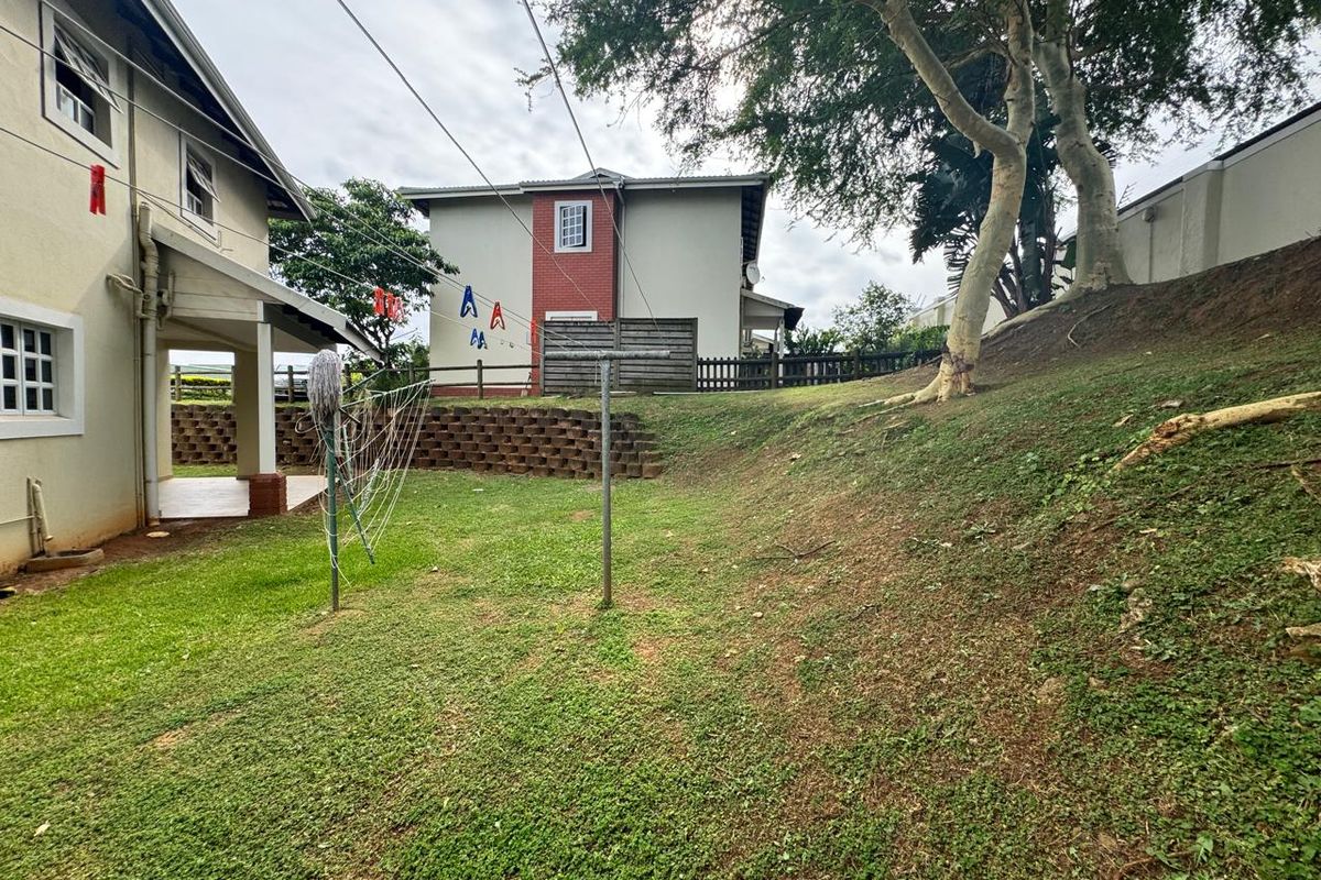 A view of the rear garden area featuring a sloped lawn, retaining wall, and a covered patio attached to the townhouse structure.