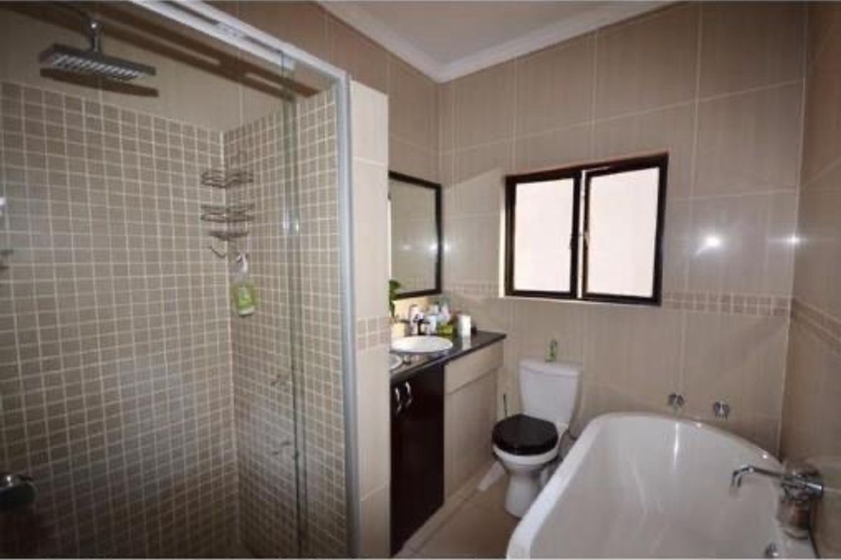 A functional bathroom featuring a glass-enclosed shower, a separate bathtub, a vanity with a basin, and a toilet with neutral wall tiling.