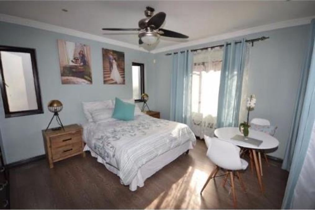 A well-lit bedroom featuring laminate flooring, a ceiling fan, and large windows with curtains, providing a comfortable and functional living space.