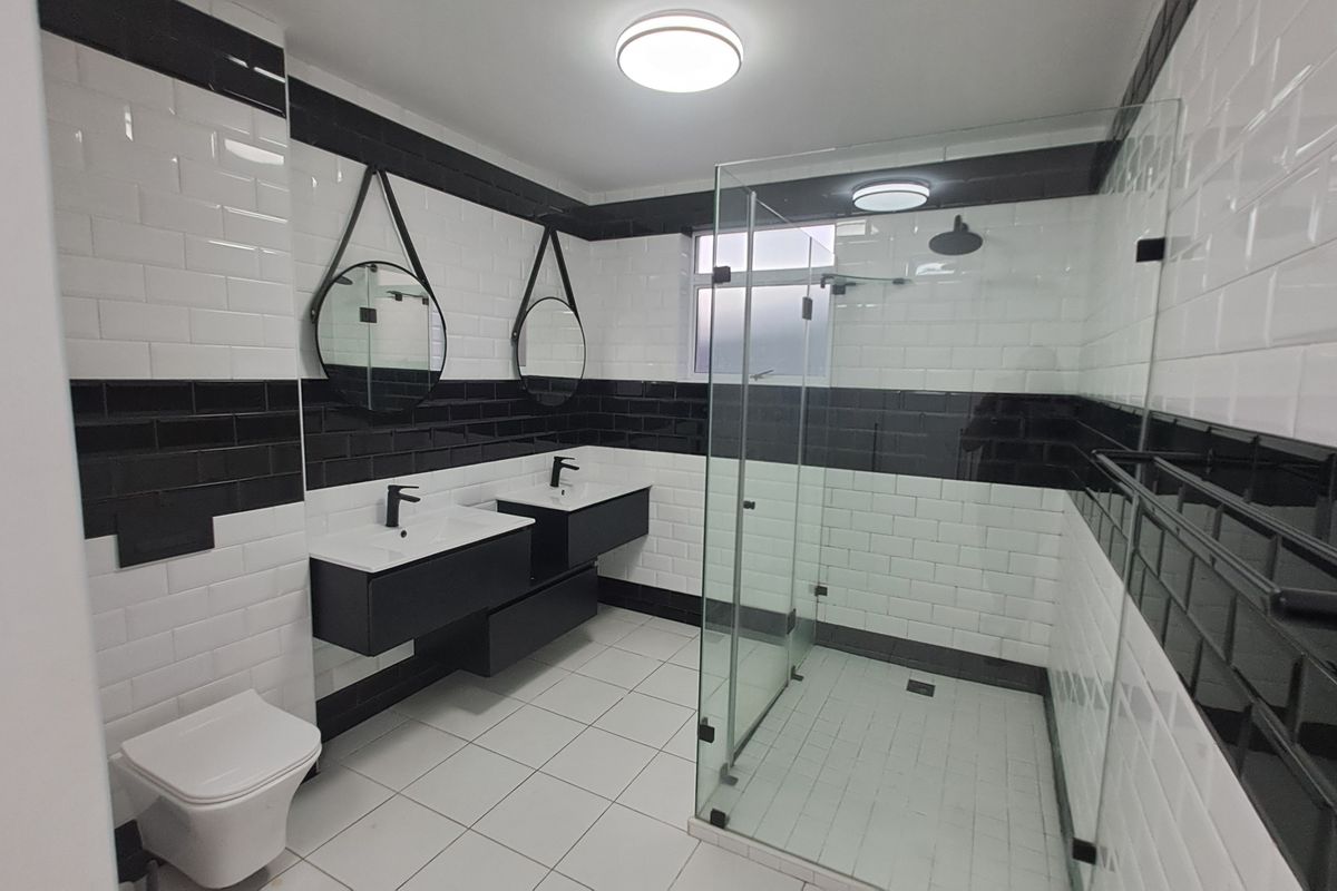 Modern bathroom featuring a double vanity with black cabinetry, a walk-in glass shower, and a striking black and white subway tile design.
