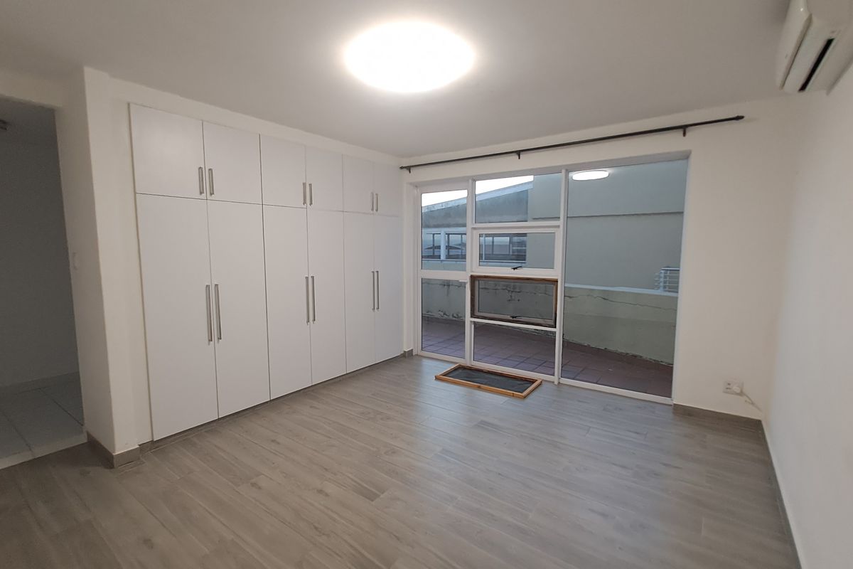 A bright bedroom featuring built-in floor-to-ceiling wardrobes, wood-look flooring, and a large glass door providing access to a private balcony.