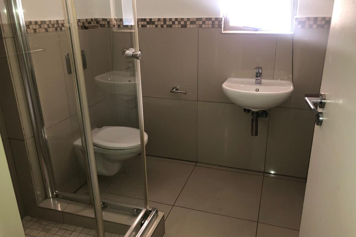 A functional bathroom featuring a glass-enclosed shower, wall-mounted basin, and toilet with neutral wall and floor tiling.