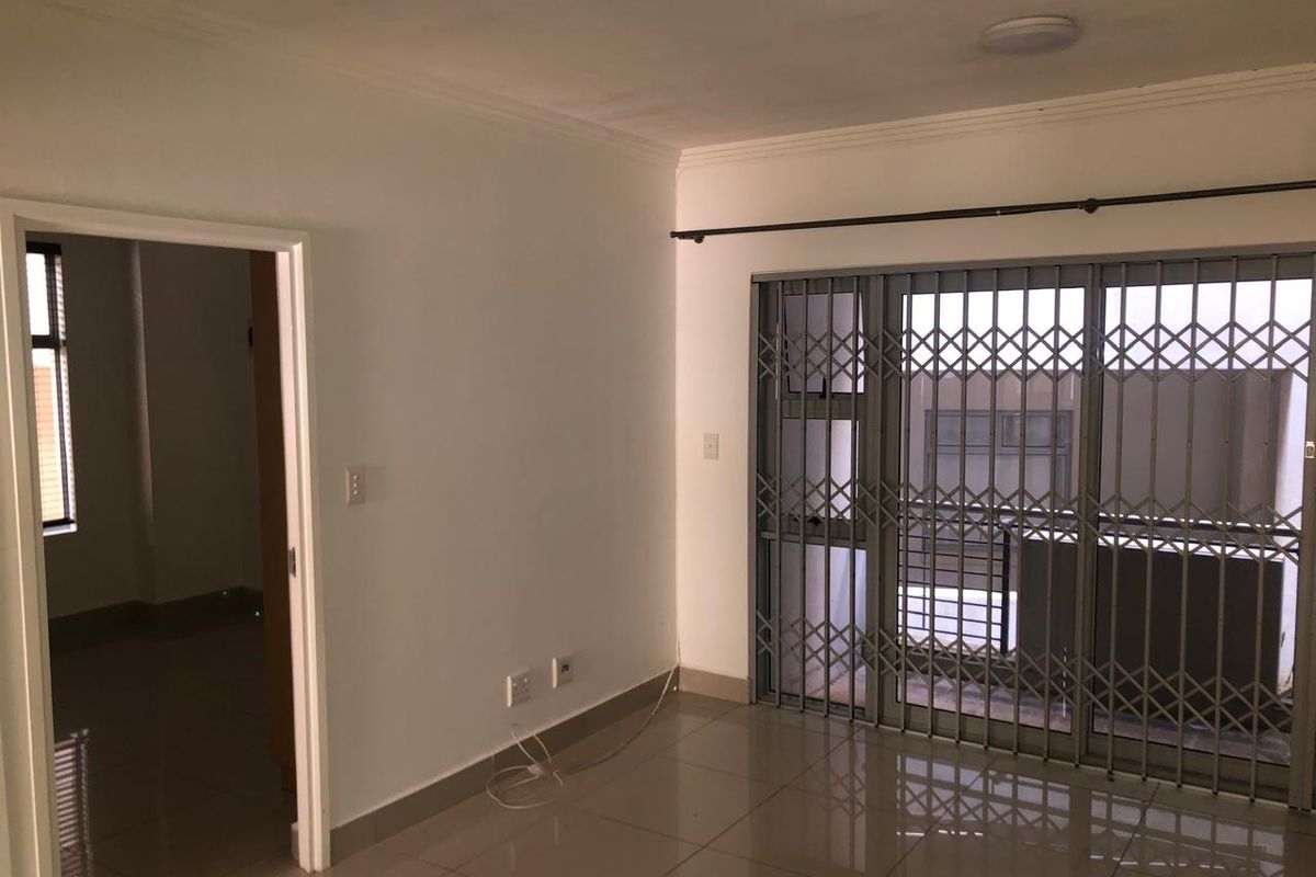 An empty living area featuring tiled flooring, a sliding door with security gate, and access to an adjacent room.