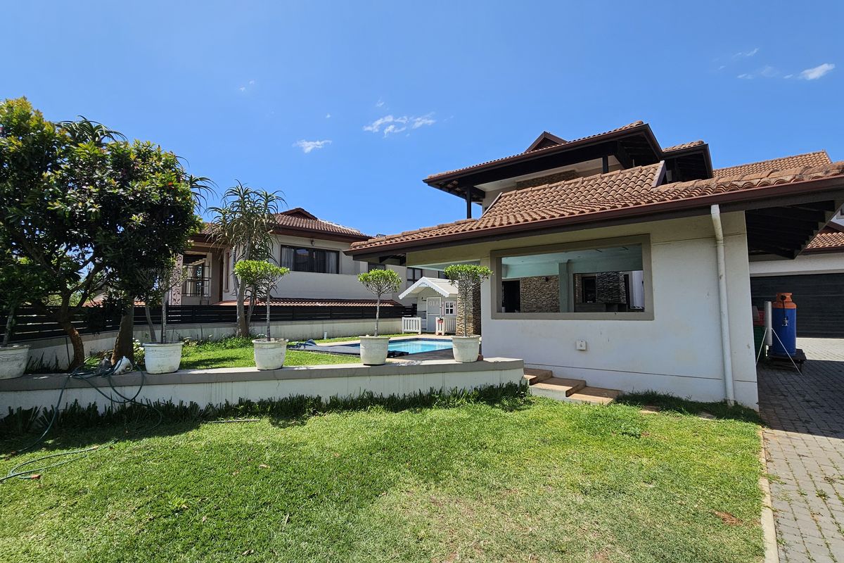 Rear view of the property featuring a landscaped garden, a swimming pool, and a covered patio area with tiled roof.