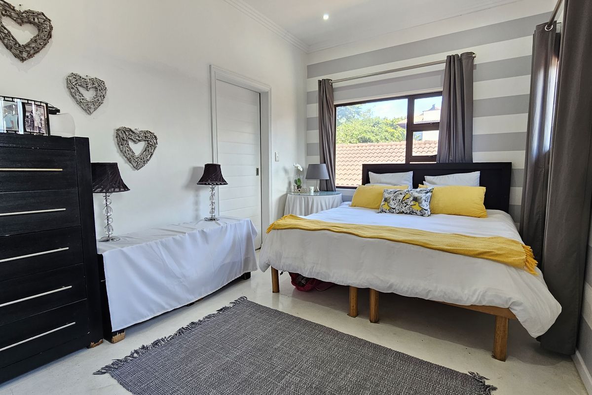 A well-lit bedroom featuring a large window, neutral tiled flooring, and a decorative striped accent wall.