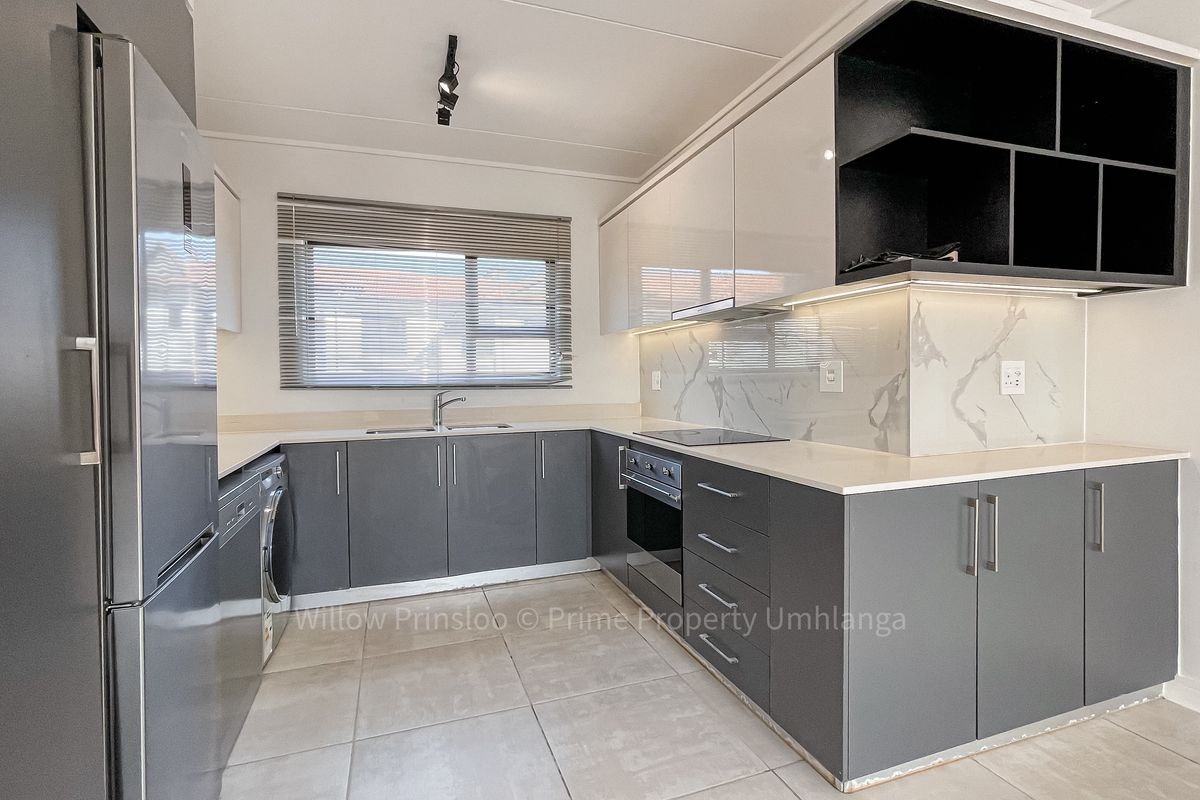 Modern kitchen featuring sleek grey cabinetry, marble-look splashback, integrated oven and hob, and tiled flooring in a contemporary apartment setting.