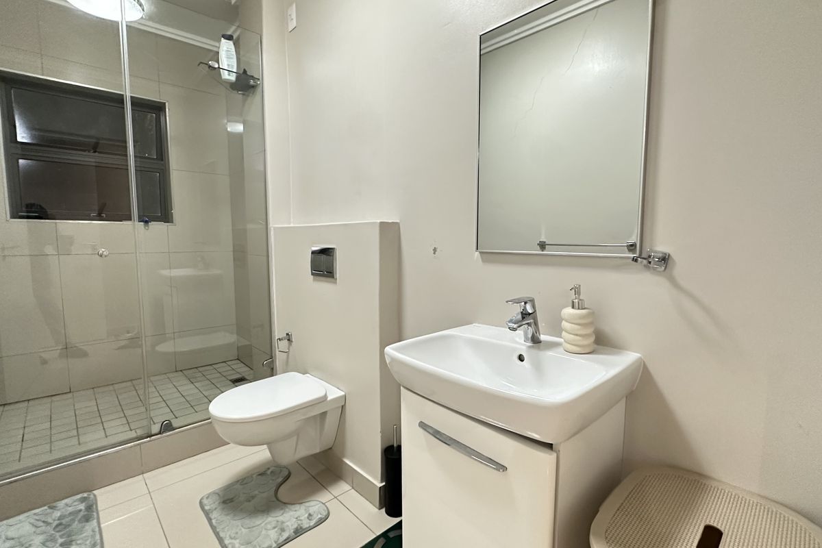 Modern bathroom featuring a glass-enclosed shower, wall-mounted toilet, and a vanity basin with a mirror.