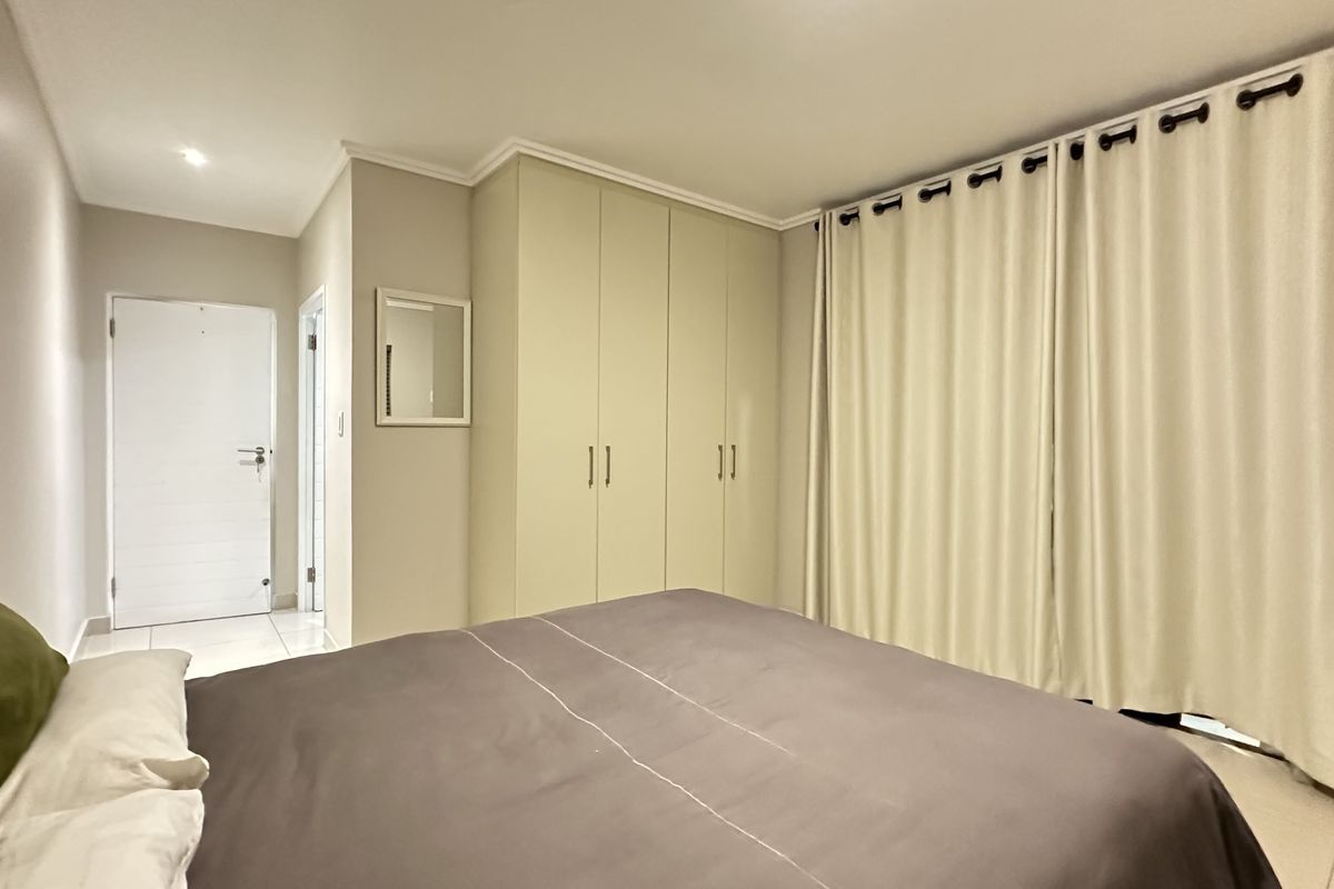 A well-maintained bedroom featuring built-in floor-to-ceiling cabinetry, neutral wall finishes, and large window curtains providing natural light control.